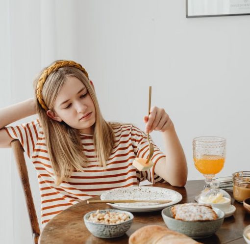 Teen girl in striped shirt at breakfast table with fruits, bread, and juice. Casual morning setting.
