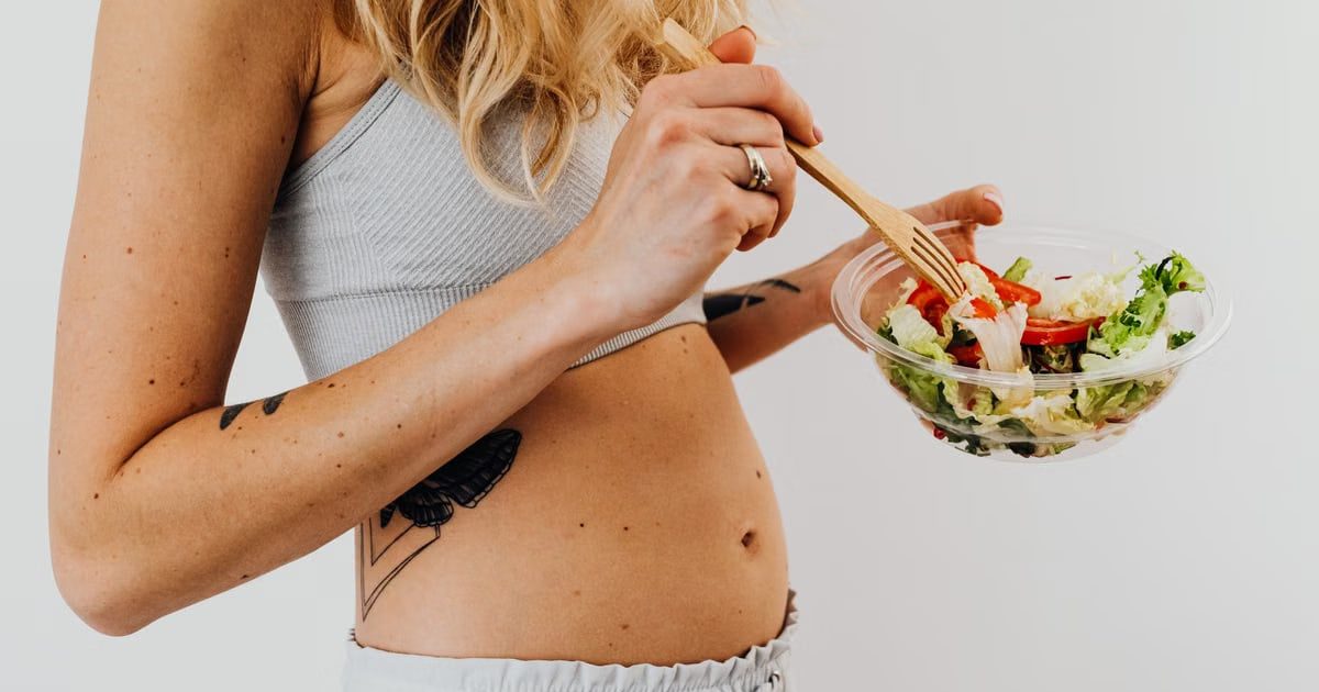 Close-up of a woman in a crop top enjoying a fresh salad indoors.