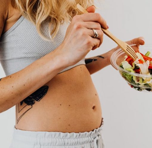 Close-up of a woman in a crop top enjoying a fresh salad indoors.