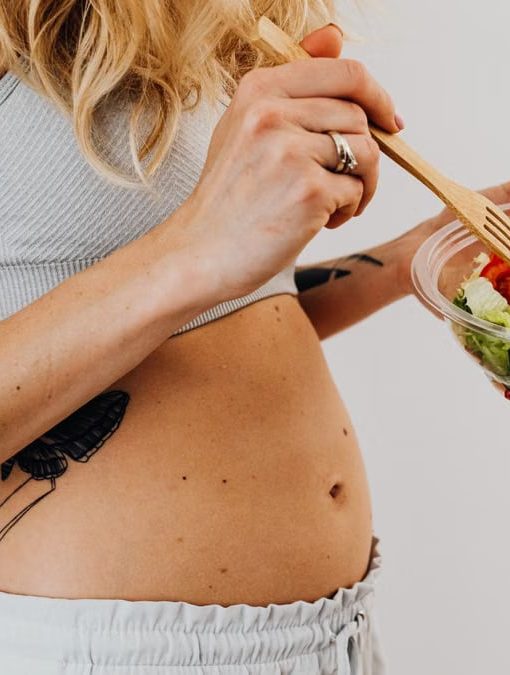Close-up of a woman in a crop top enjoying a fresh salad indoors.