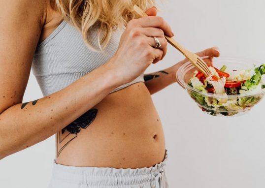 Close-up of a woman in a crop top enjoying a fresh salad indoors.