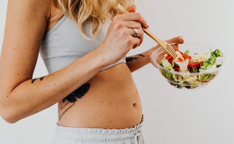 Close-up of a woman in a crop top enjoying a fresh salad indoors.